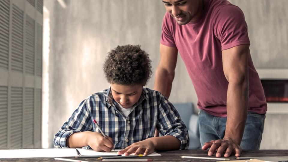 Young son sat at desk with father looking over his shoulder